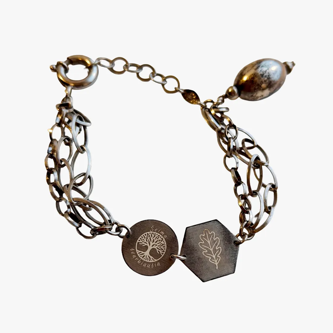 Graviravimas ant sidabrinės apyrankės su personalizuotais pakabukais ir simboliais.